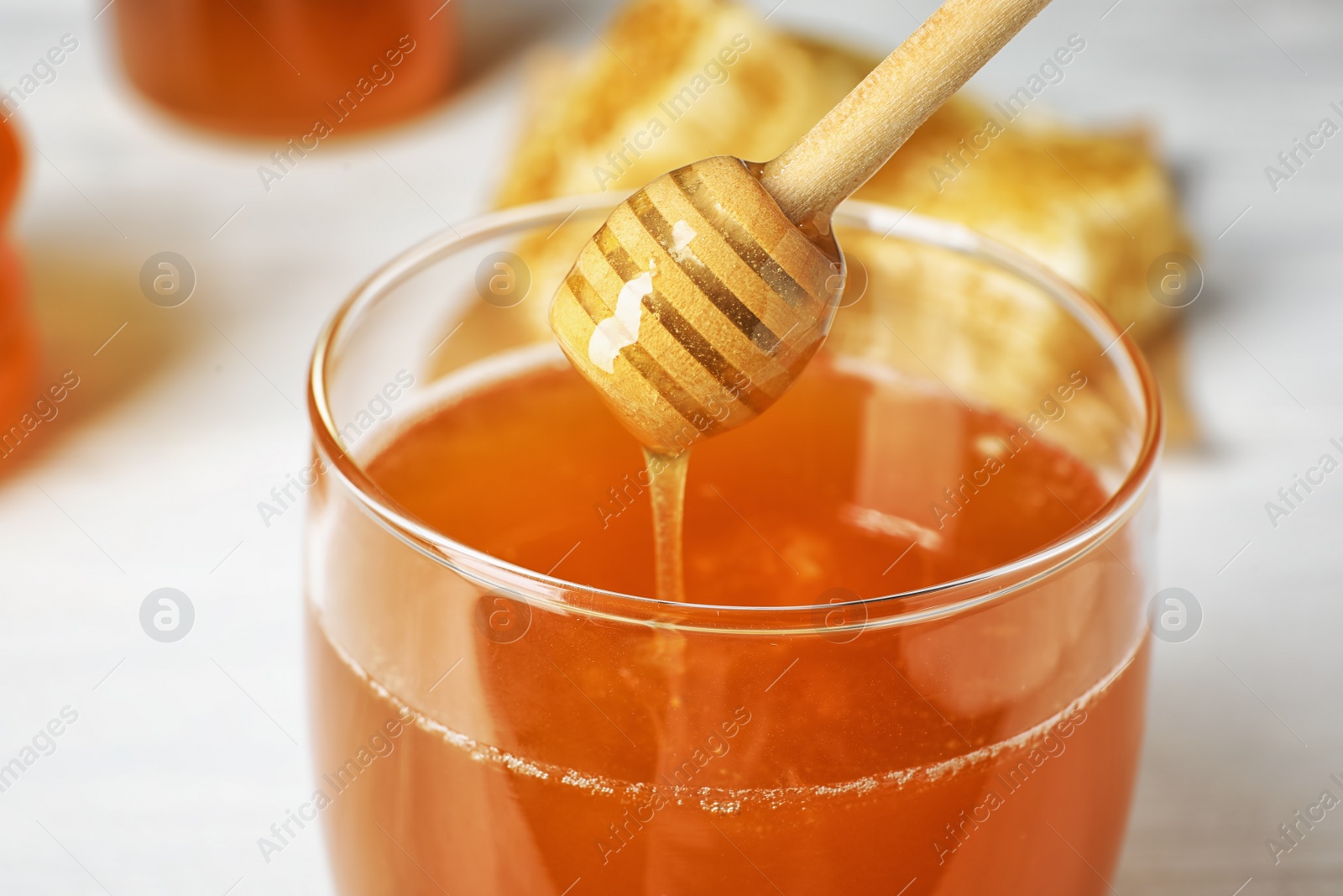 Photo of Sweet honey dripping from dipper into glass jar, closeup