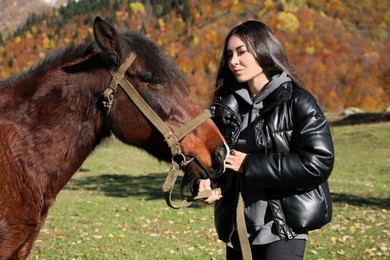 Photo of Young woman stroking horse in mountains on sunny day. Beautiful pet