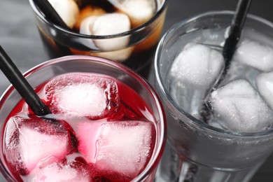 Glasses of different refreshing soda water with ice cubes and straws on grey table, closeup