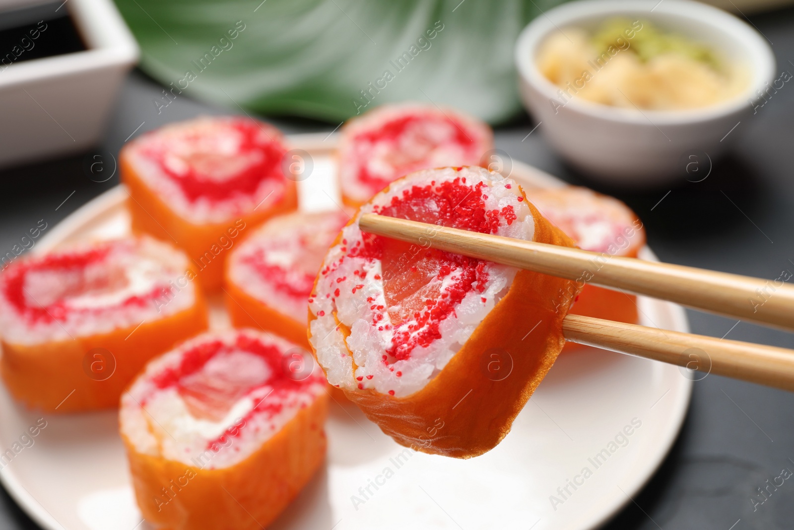 Photo of Holding delicious sushi roll with chopsticks at grey table, closeup