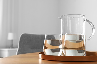 Photo of Tray with jug and glasses of water on wooden table in room, space for text. Refreshing drink