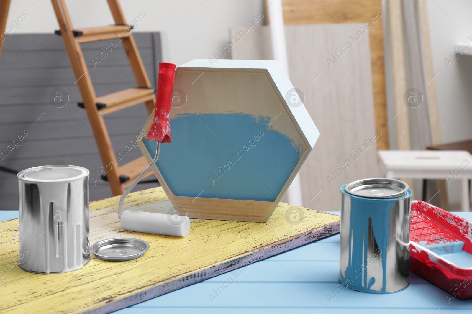 Photo of Cans of paint, roller and tray on blue wooden table indoors