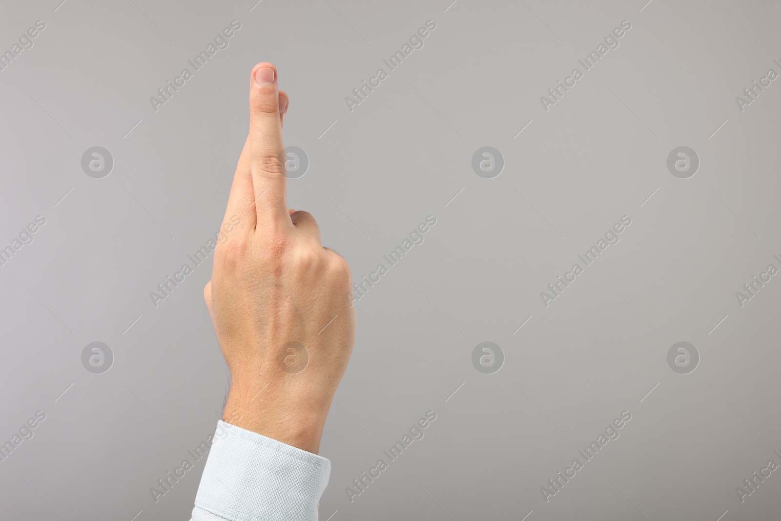 Photo of Man crossing his fingers on grey background, closeup. Space for text