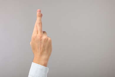 Photo of Man crossing his fingers on grey background, closeup. Space for text