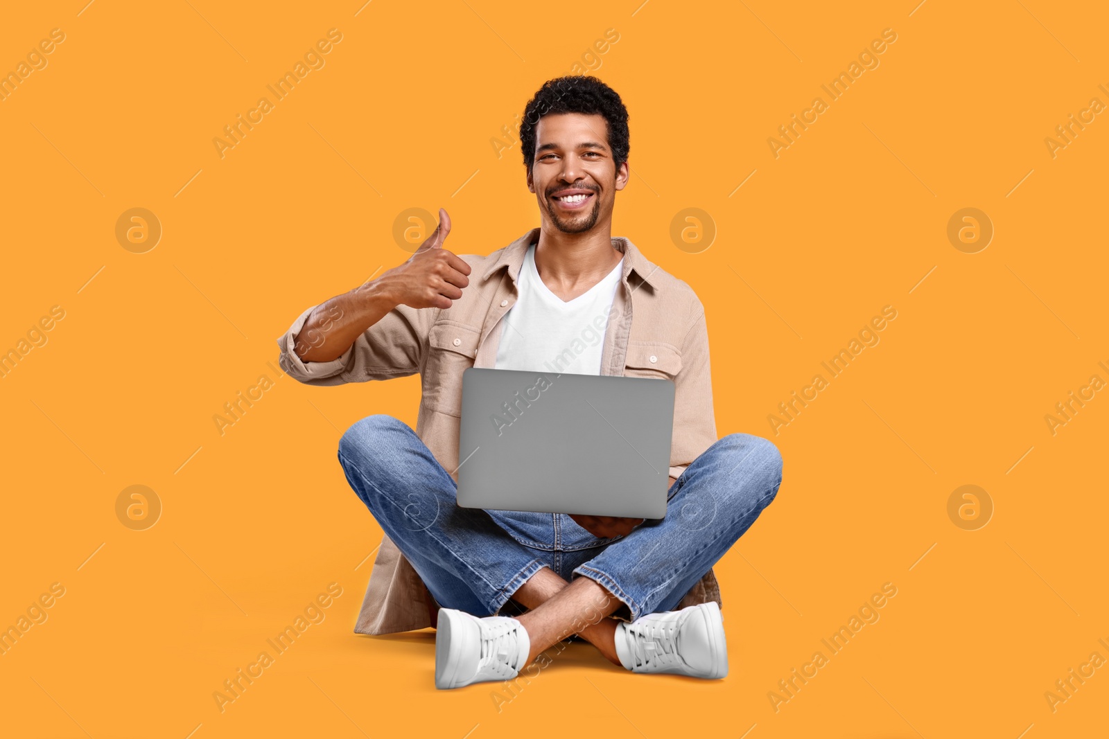 Photo of Happy man with laptop showing thumb up against orange background