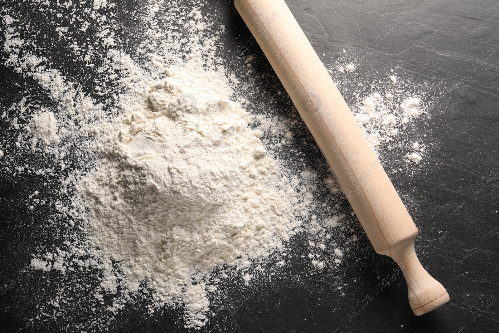 Photo of Pile of flour and rolling pin on black textured table, top view