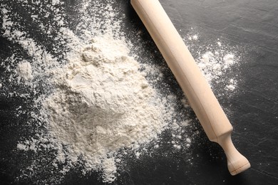 Pile of flour and rolling pin on black textured table, top view