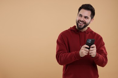 Photo of Happy young man using smartphone on beige background, space for text