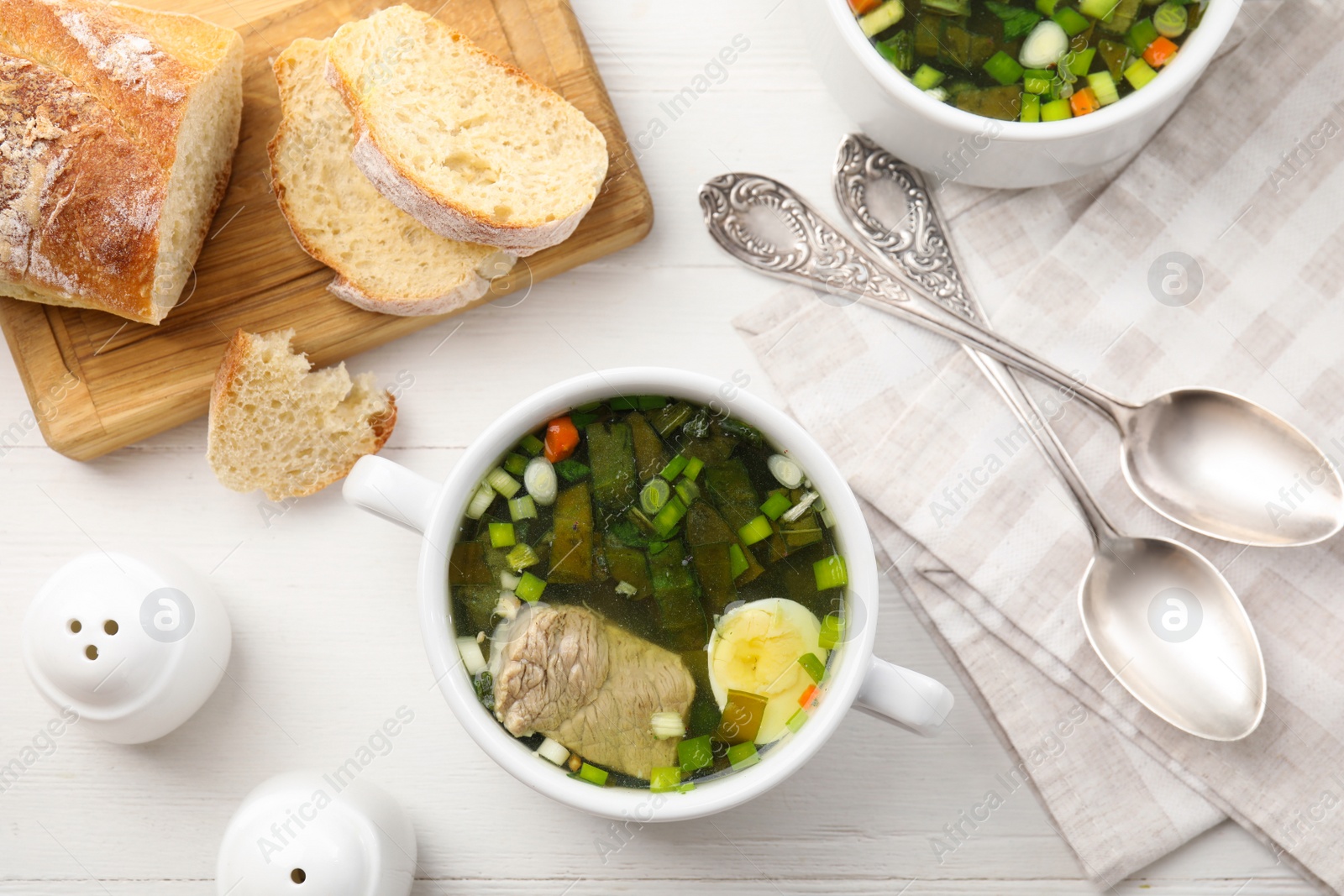 Photo of Delicious sorrel soup with meat and egg served on white wooden table, flat lay