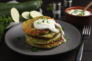 Photo of Delicious zucchini fritters with sour cream on wooden table