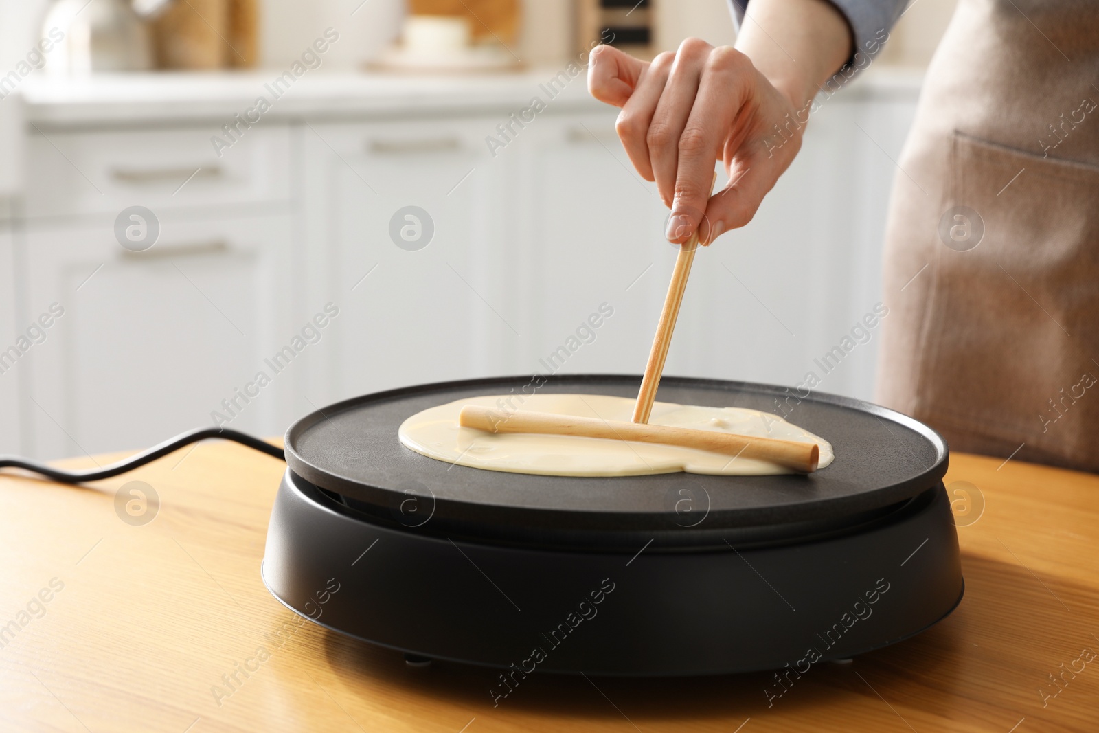 Photo of Woman cooking delicious crepe on electrical pancake maker in kitchen, closeup