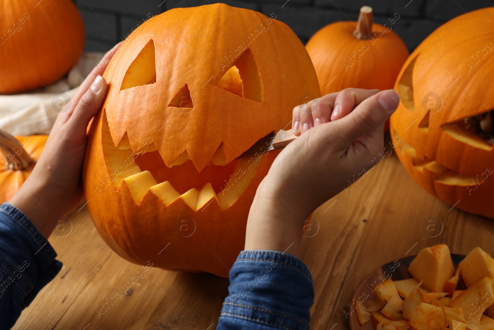 Photo of Woman carving pumpkin at wooden table, closeup. Halloween celebration