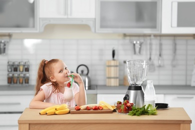 Photo of Little girl with glass of delicious milk shake in kitchen