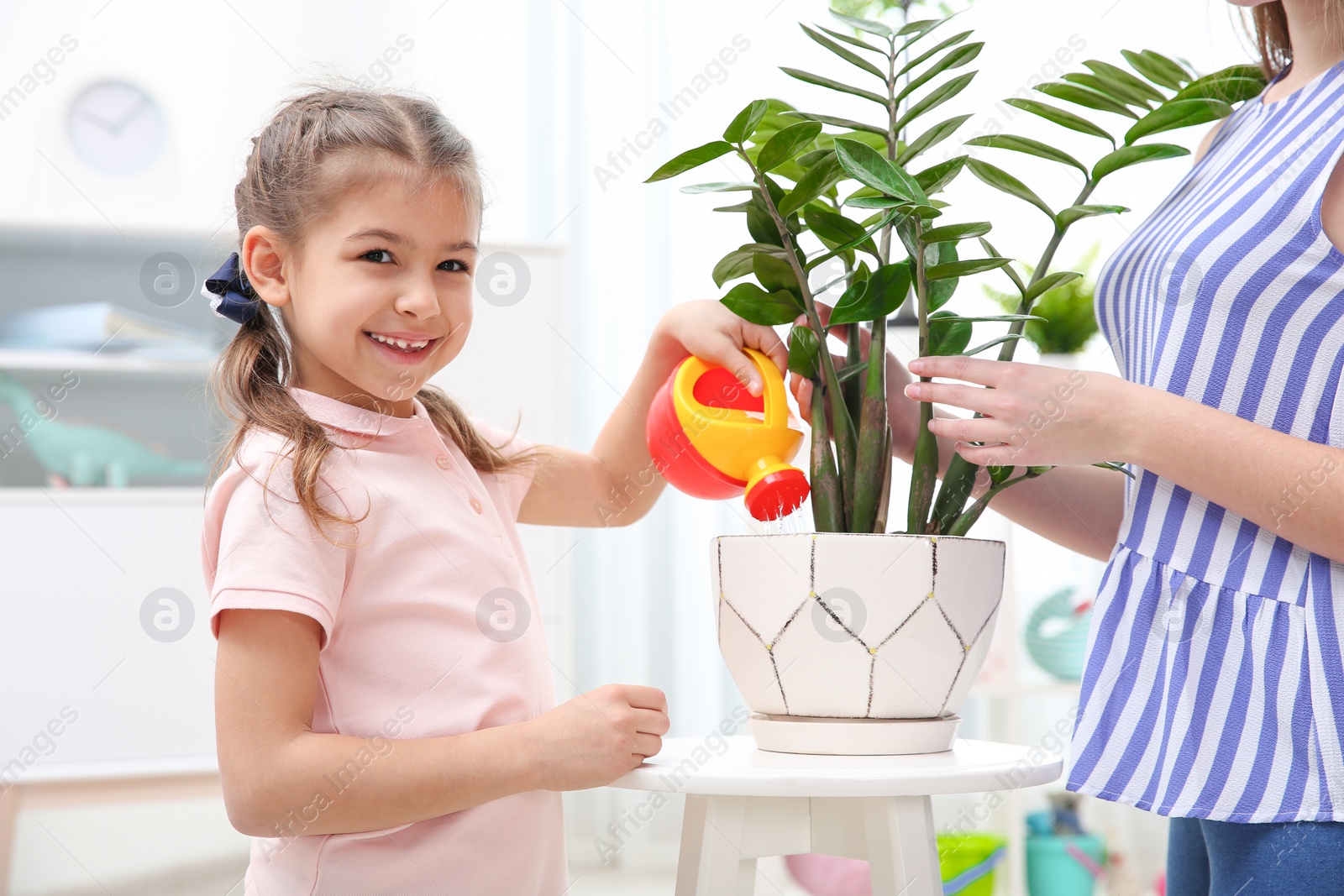 Photo of Child with toy watering can helping mother to take care of houseplant at home. Playing indoors