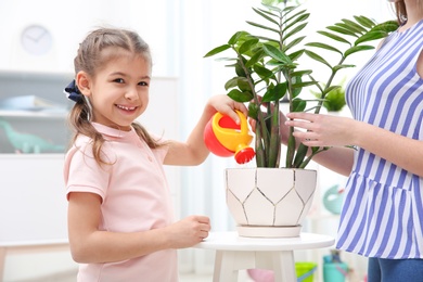 Child with toy watering can helping mother to take care of houseplant at home. Playing indoors