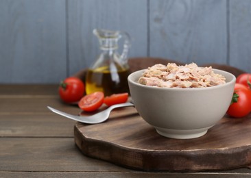 Bowl with canned tuna and tomatoes on wooden table, space for text