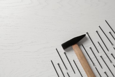 Hammer and metal nails on white wooden table, flat lay. Space for text