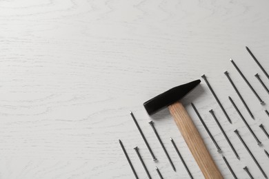 Photo of Hammer and metal nails on white wooden table, flat lay. Space for text