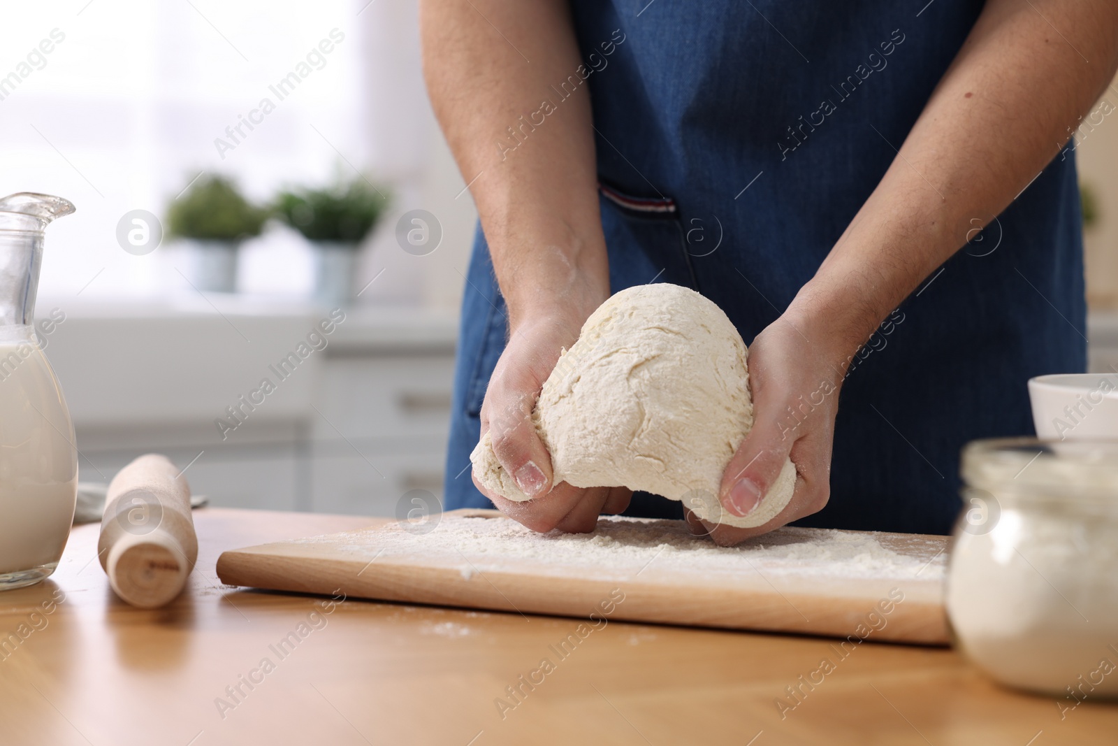 Photo of Making bread. Man kneading dough at wooden table in kitchen, closeup