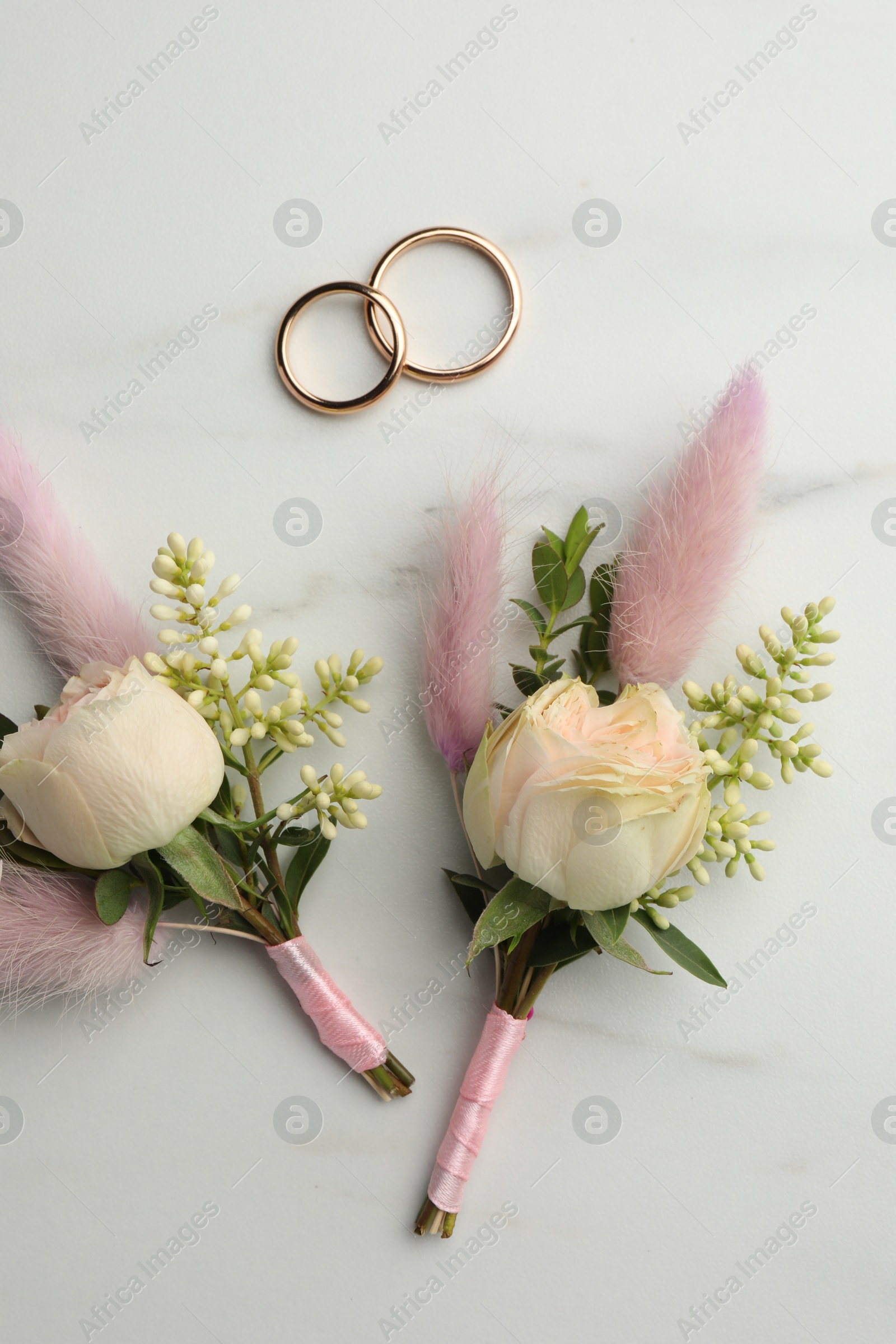 Photo of Small stylish boutonnieres and rings on white marble table, flat lay