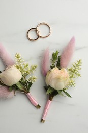 Small stylish boutonnieres and rings on white marble table, flat lay