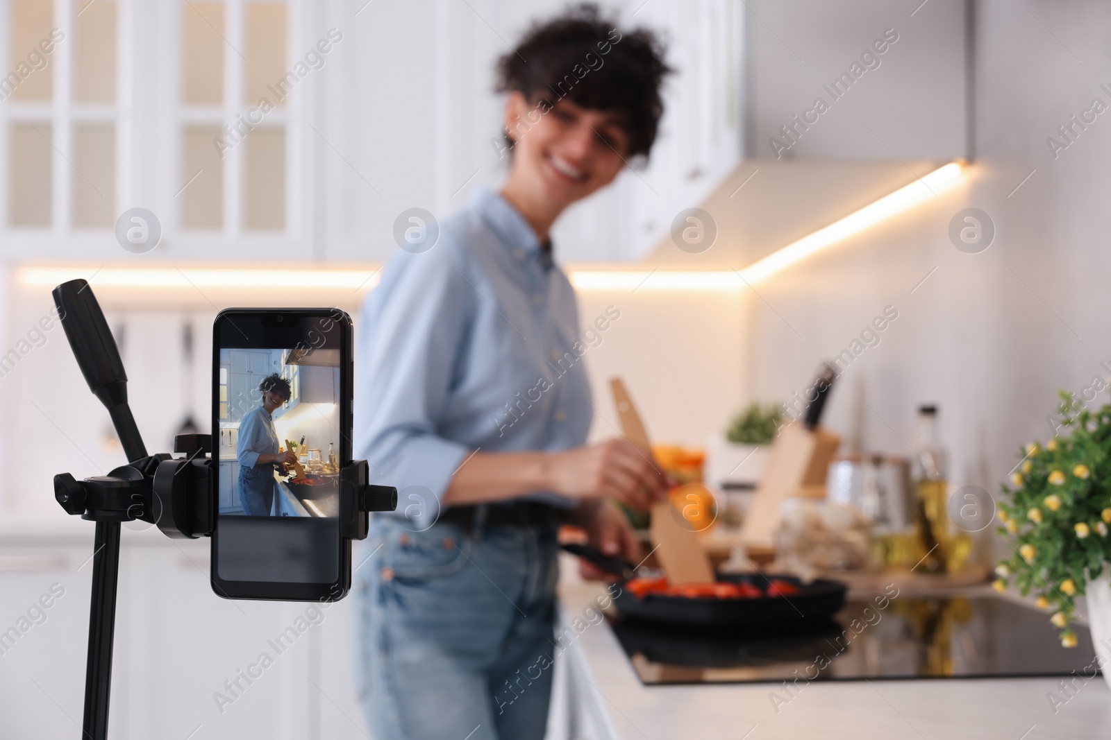 Photo of Food blogger cooking while recording video in kitchen, focus on smartphone
