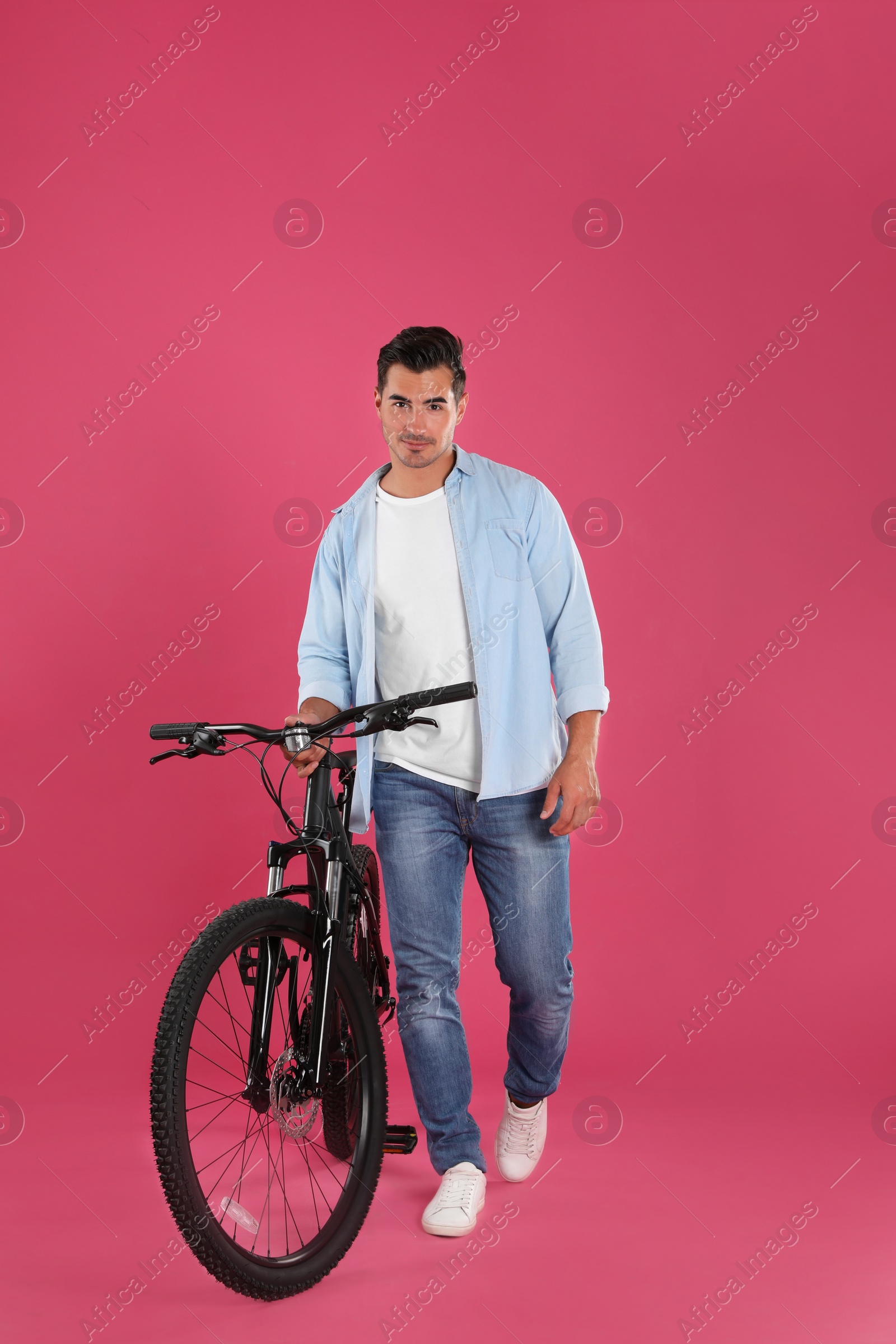 Photo of Handsome young man with modern bicycle on pink background