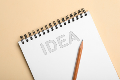 Image of Notebook with word IDEA and pencil on beige background, top view