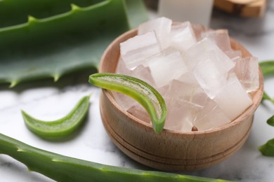 Photo of Aloe vera gel and slices of plant on white table, closeup