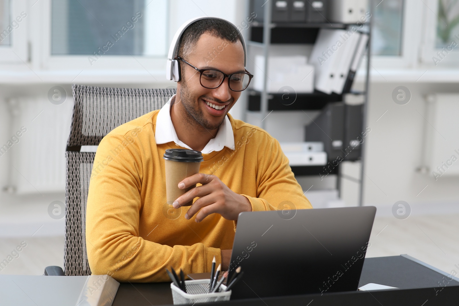 Photo of Young man with cup of drink working on laptop at table in office