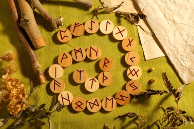 Photo of Many wooden runes and dried plants on olive fabric, flat lay