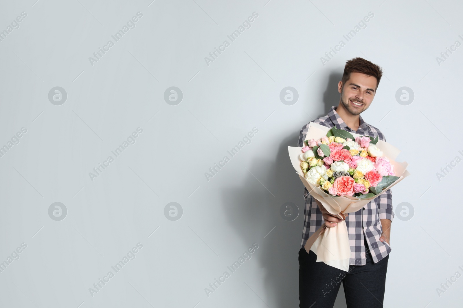 Photo of Young handsome man with beautiful flower bouquet on light background, space for text