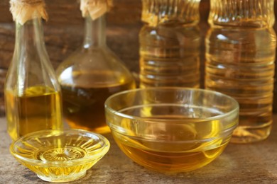 Photo of Glass bowls and bottles with sunflower oil on wooden table, closeup