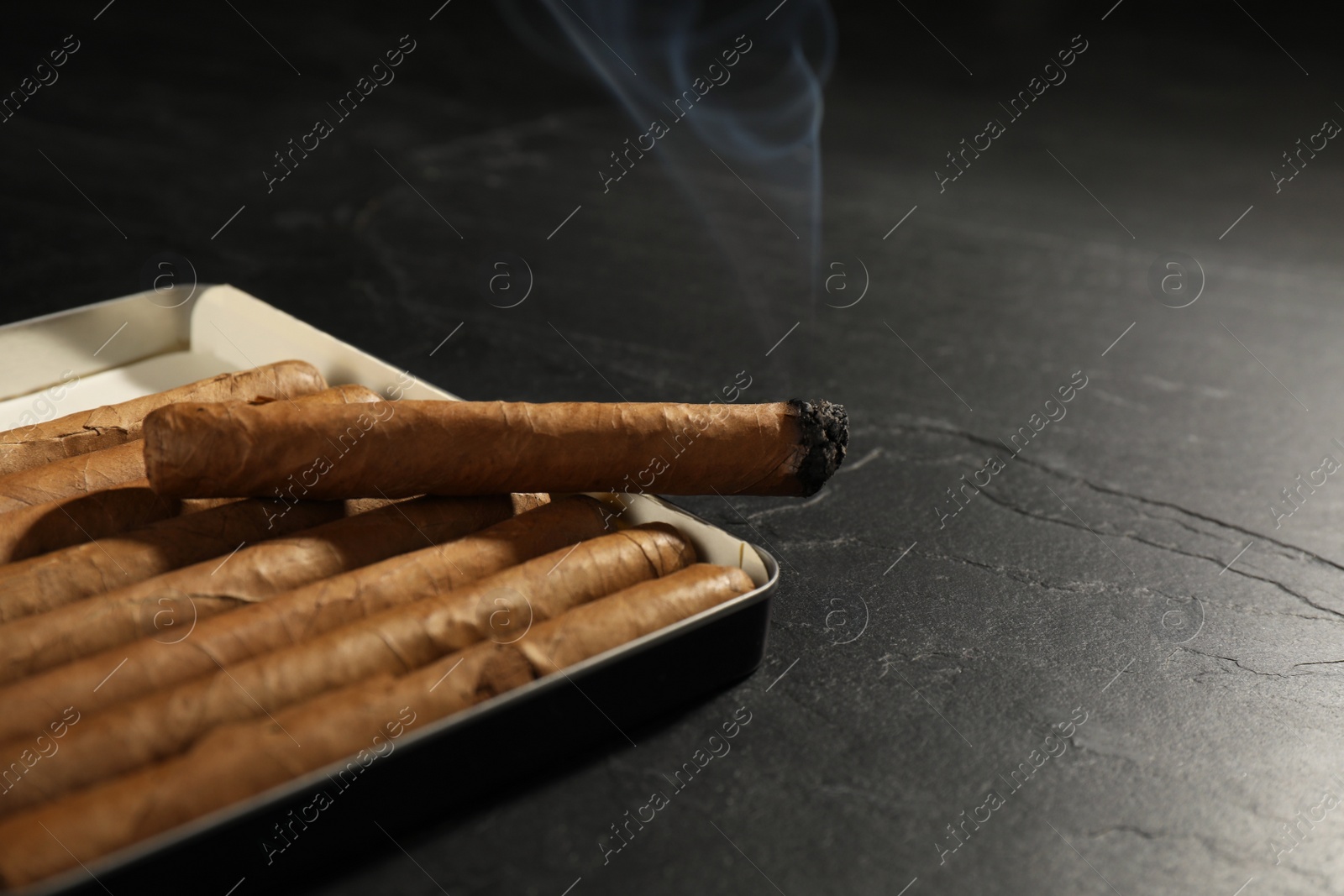 Photo of Many cigars in box on black table, closeup