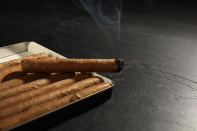 Photo of Many cigars in box on black table, closeup