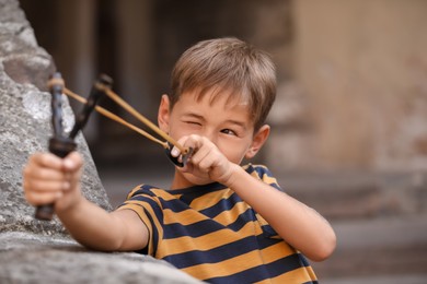 Photo of Cute little boy playing with slingshot outdoors