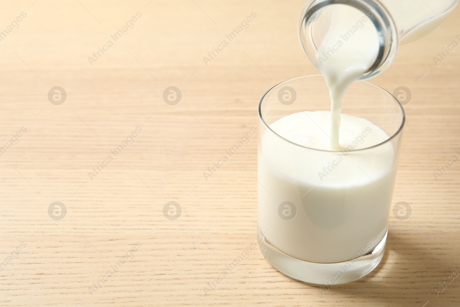 Photo of Pouring milk into glass on wooden table. Space for text