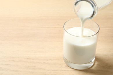 Pouring milk into glass on wooden table. Space for text