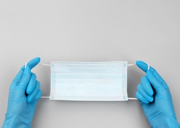 Doctor in medical gloves holding protective mask on light grey background, closeup. Space for text