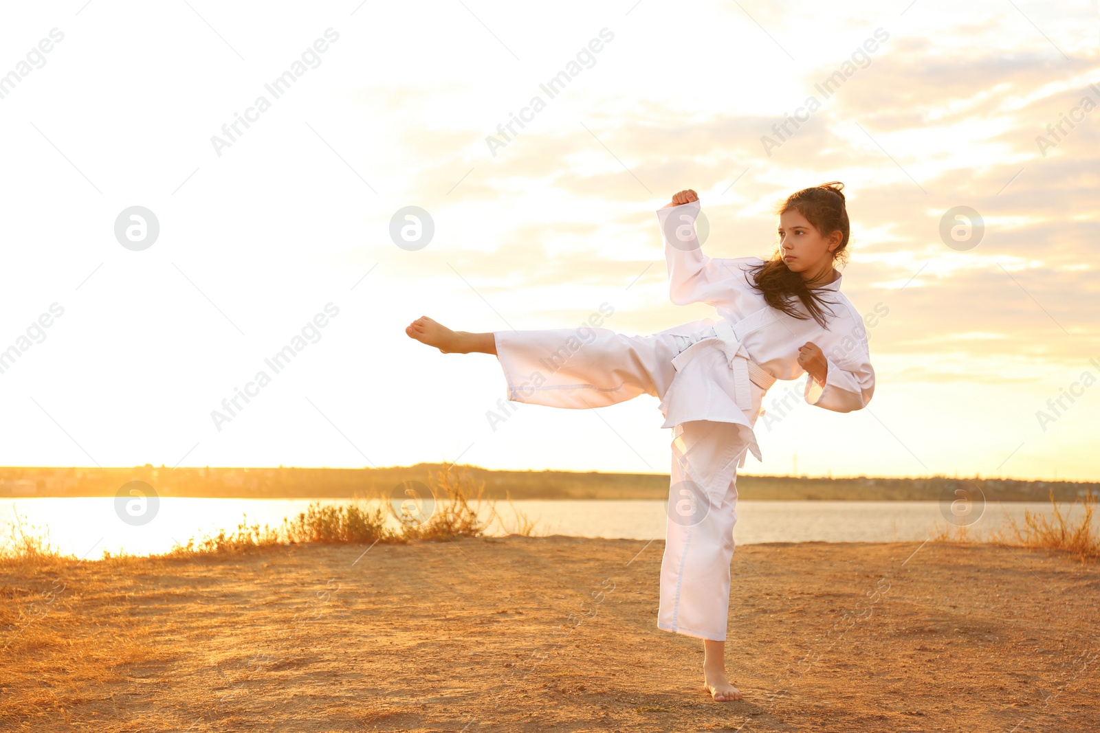 Photo of Cute little girl in kimono practicing karate near river at sunset