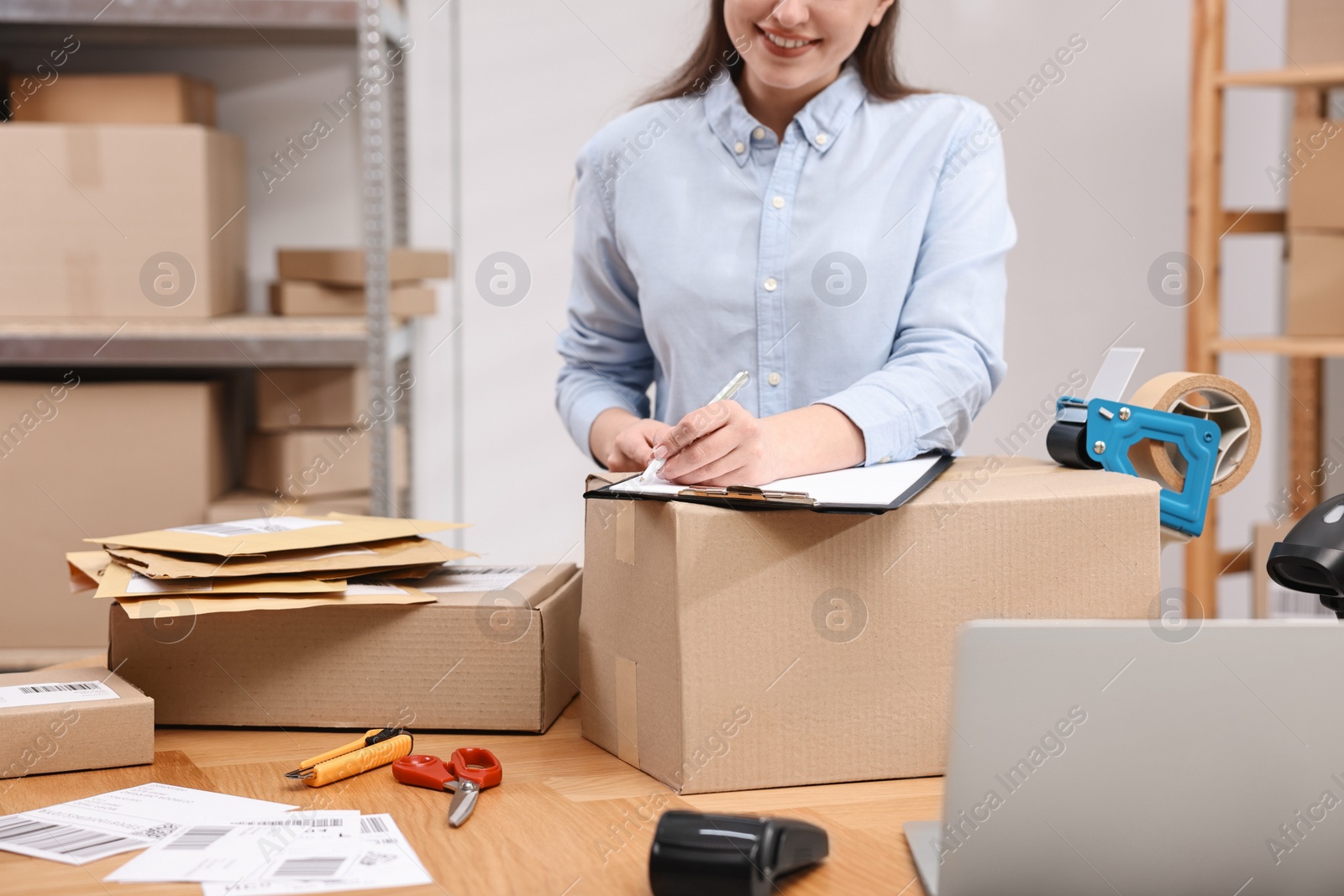 Photo of Parcel packing. Post office worker with clipboard writing notes at wooden table indoors, closeup