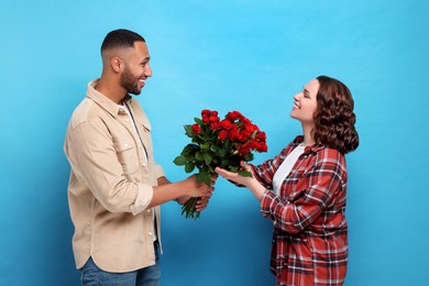 Photo of Boyfriend presenting bouquet of red roses to his girlfriend on light blue background. Valentine's day celebration