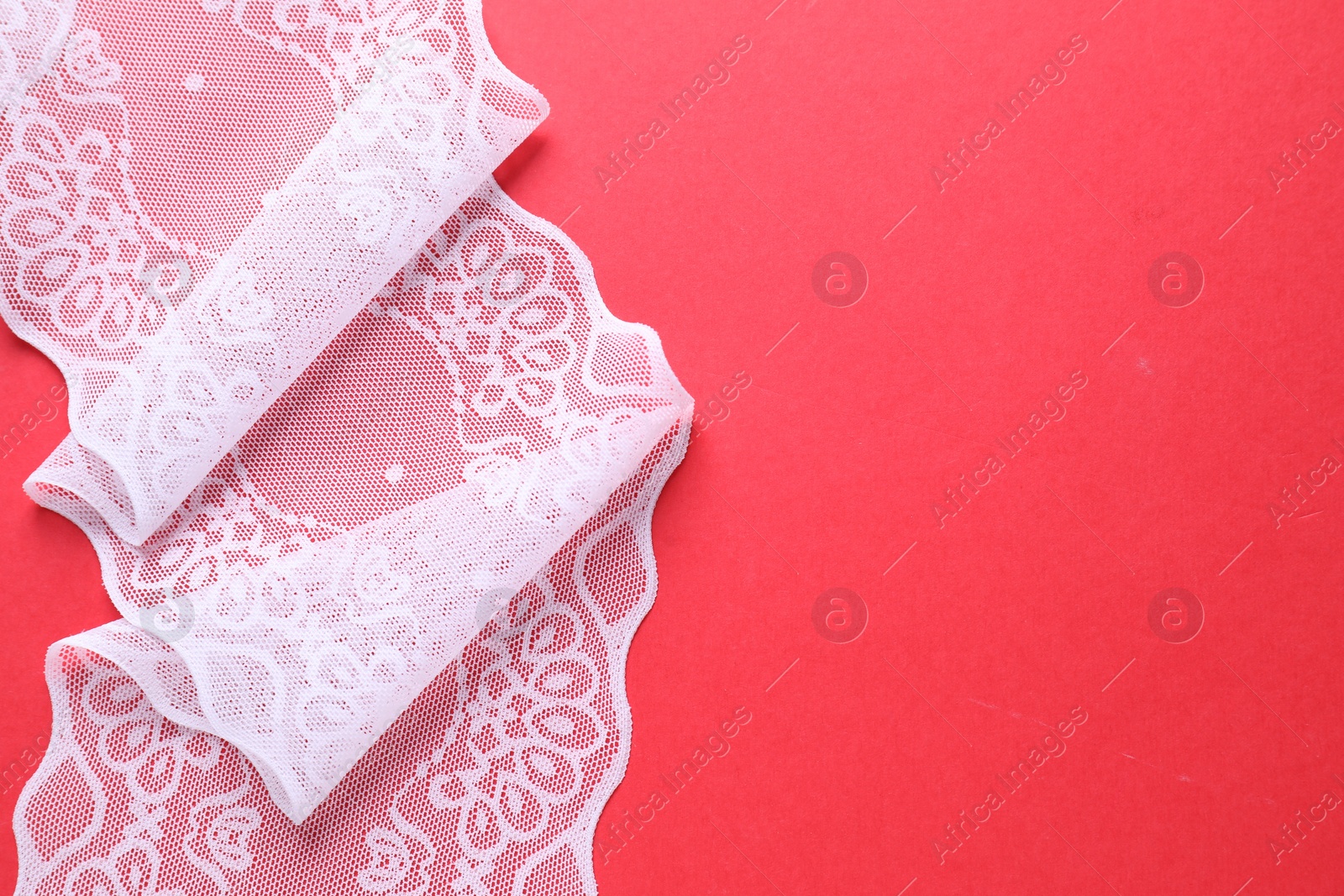 Photo of White lace on red background, top view. Space for text