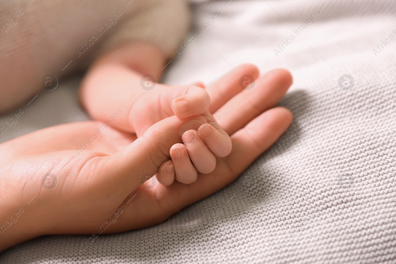 Photo of Mother and her newborn baby on light grey knitted plaid, closeup