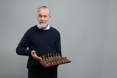 Man with chessboard and game pieces on light gray background, space for text