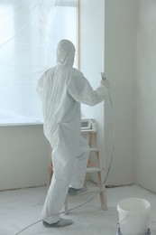 Decorator painting window slope on ladder indoors, back view