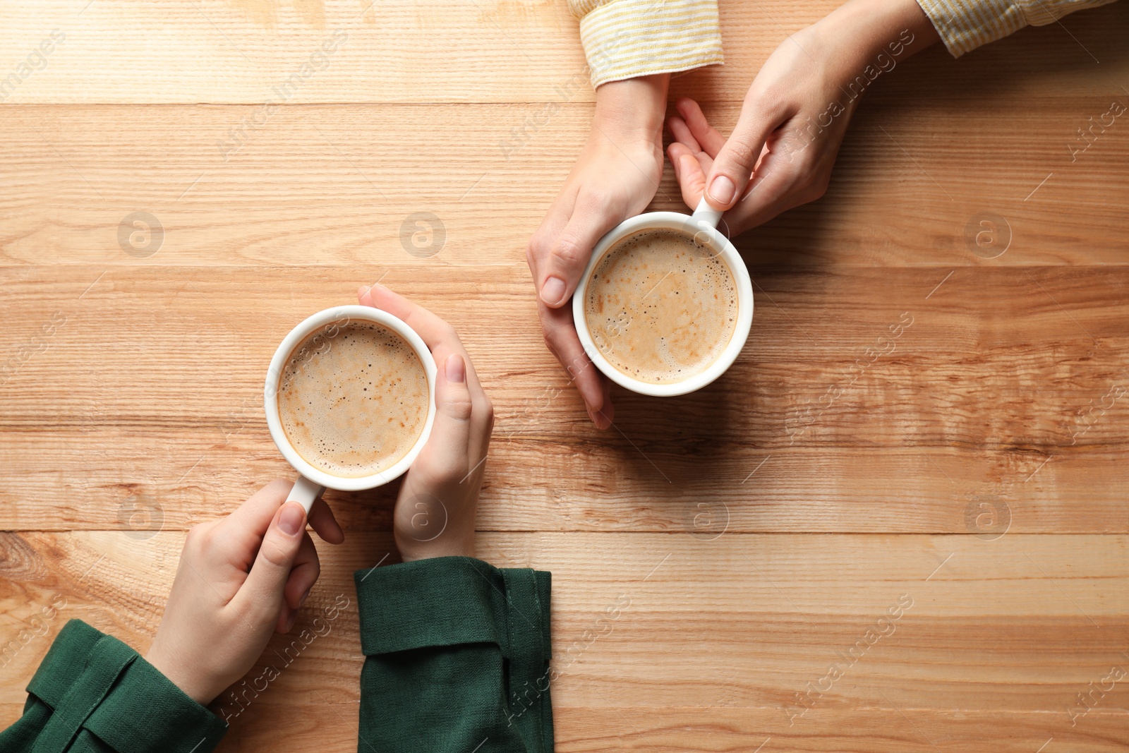 Photo of Women with cups of coffee at wooden table, top view