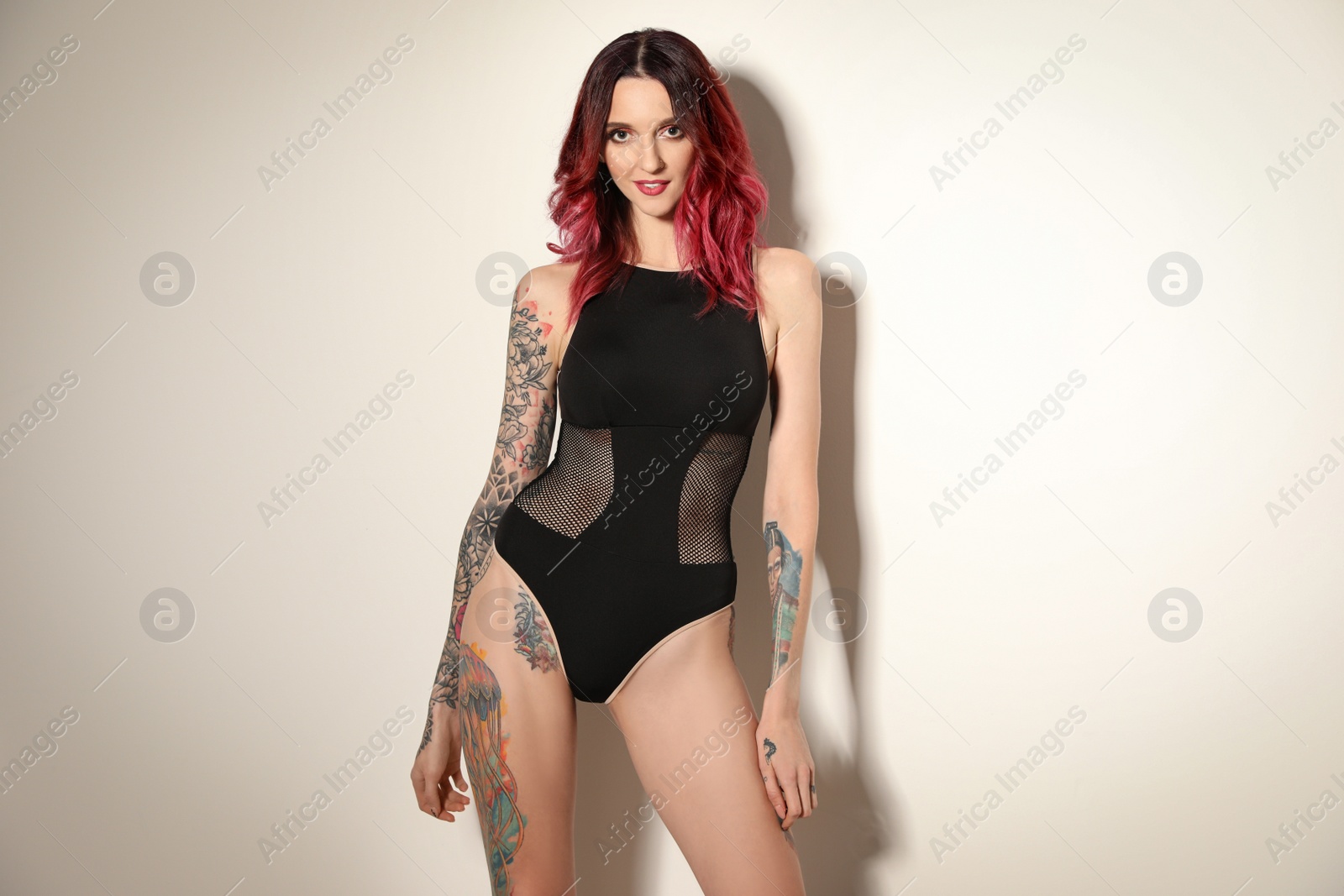 Photo of Beautiful woman with tattoos on body against light background