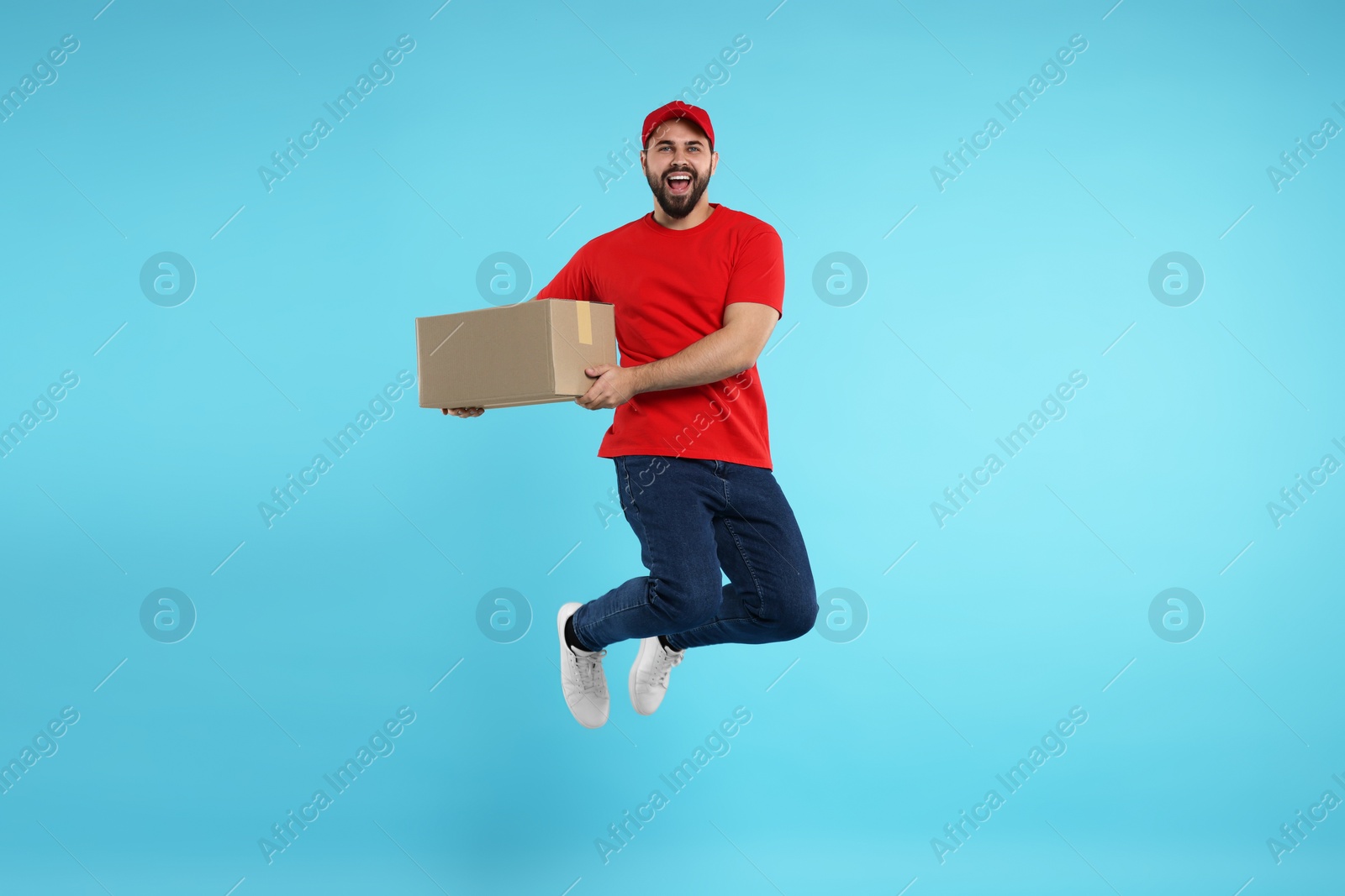 Photo of Happy young courier with parcel jumping on light blue background