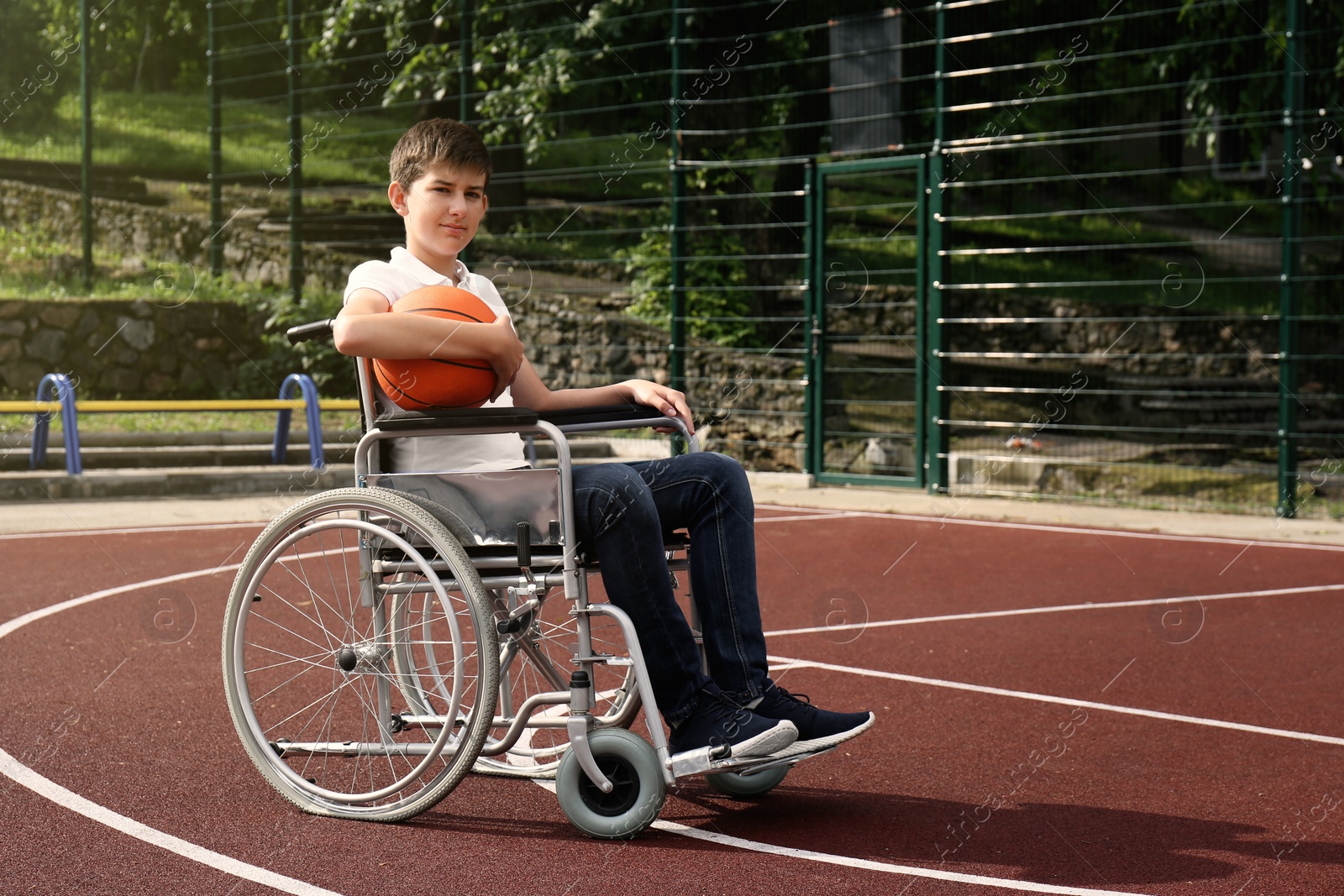 Photo of Disabled teenage boy in wheelchair with basketball ball at outdoor court